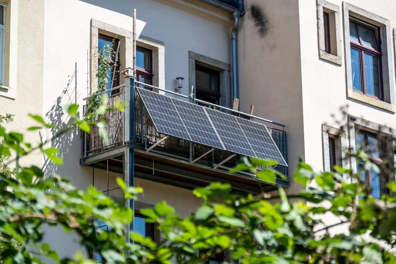 Ansicht auf einen Balkon durch Blätter hindurch. Der Balkon hat PV-Panele für die erzeugung von Strom montiert